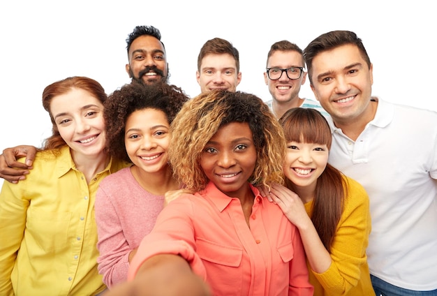 Foto diversidade, raça, etnia, tecnologia e conceito de pessoas - grupo internacional de homens e mulheres sorridentes felizes tirando selfie sobre branco