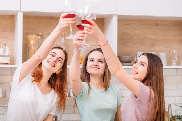 Diversión de fiesta de chicas. Celebrando a las mujeres. Felices hembras jóvenes tintineo copas de vino tinto.