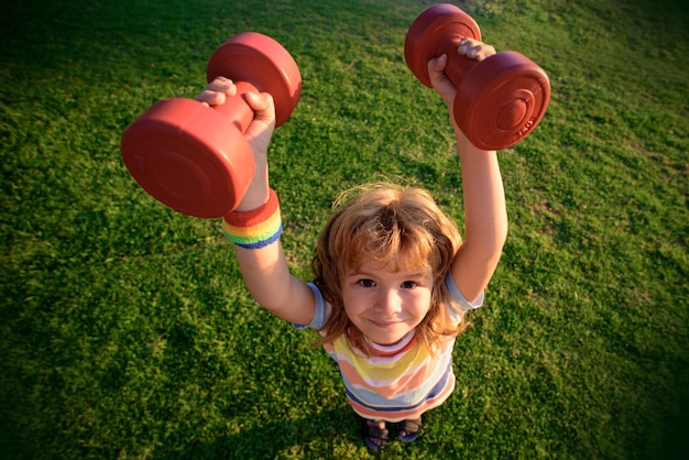 Diversión física, entrenamiento de niño pequeño afuera. Niño divertido con pesas.