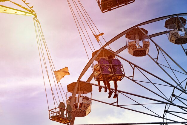 Foto diversión en el lunapark, gente en la montaña rusa y la gran rueda, puesta de sol