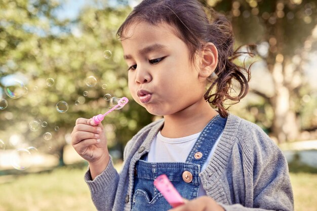 Diversión en la naturaleza y una niña haciendo burbujas en un parque al aire libre en un feliz fin de semana de verano Diversión al sol y una burbuja de jabón libertad jugando en el jardín un niño lindo en el campo con árboles y sol