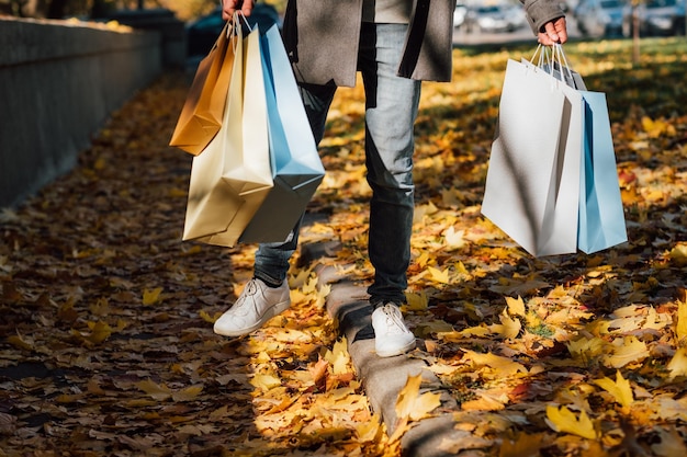 Diversión de otoño Captura recortada de un hombre caminando con bolsas de compras disfrutando de la temporada de otoño con hojas amarillas que cubren la acera