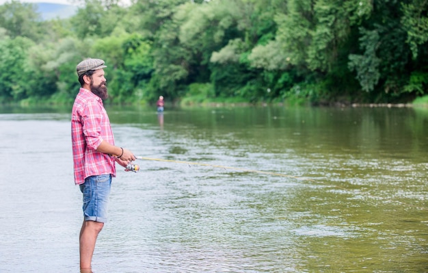 La diversión de pescar es atrapar Fisher con equipo de pesca Pescar en el anzuelo Hombre brutal usar botas de goma pararse en el agua del río Actividad de fin de semana de Fisher Ocio en la naturaleza salvaje Pesca pasatiempo masculino