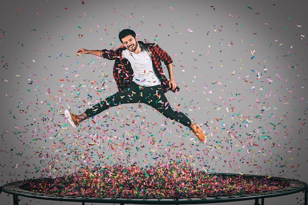 Diversión sin preocupaciones. Toma en el aire de un joven apuesto saltando en un trampolín con confeti a su alrededor