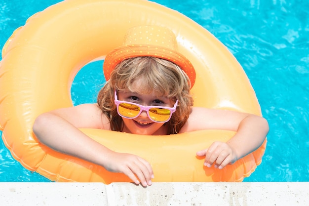 Diversión de verano Niño nadando en la piscina jugar con anillo flotante Niño lindo sonriente en gafas de sol nadar con anillos inflables en la piscina en el día de verano