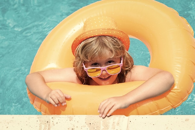 Diversión de verano Niño nadando en la piscina jugar con anillo flotante Niño lindo sonriente en gafas de sol nadar con anillos inflables en la piscina en el día de verano