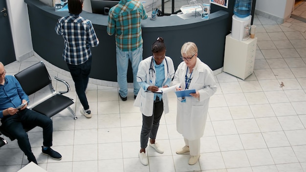 Diverso equipo médico de médicos hablando y escribiendo informes en el área de recepción del hospital, trabajando en el sistema de salud para apoyar a los pacientes enfermos. Citas en el vestíbulo de la sala de espera.