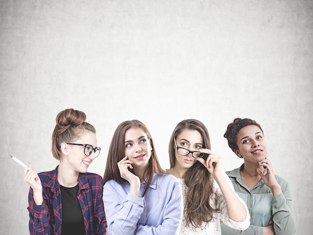 Foto diverso equipo de mujeres jóvenes con gafas y diferentes ropas y peinados de pie hombro con hombro. un fondo de pared de hormigón simulado.