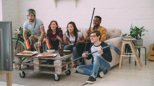 Foto diverso grupo de amigos aficionados al deporte con banderas nacionales alemanas viendo juegos de deportes de invierno en la televisión