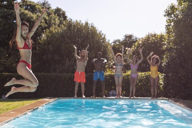 Diverso grupo de amigos divirtiéndose y saltando al agua en una fiesta en la piscina. Pasar el rato y relajarse al aire libre en verano.