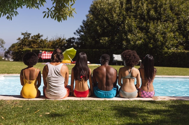 Diverso grupo de amigos sentados junto a la piscina en un día soleado. Pasar el rato y relajarse al aire libre en verano.