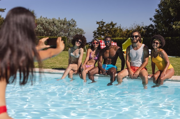 Diverso grupo de amigos tomando fotos y sentados junto a la piscina. pasar el rato y relajarse al aire libre en verano.