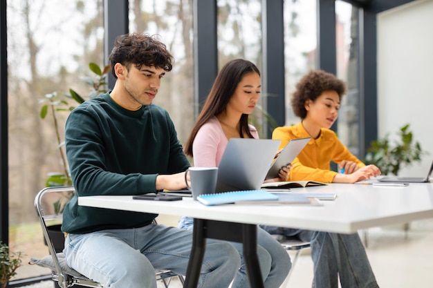 Diverso grupo de estudiantes sentados en la biblioteca universitaria con aparatos aprendiendo para hacer exámenes