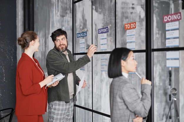 Diverso grupo de gente de negocios de pie junto a la pared de vidrio mientras planifica el proyecto en la oficina moderna, espacio de copia