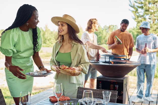 Diverso grupo de jóvenes disfrutando de una fiesta de barbacoa al aire libre en sumer se centran en dos mujeres sonrientes s