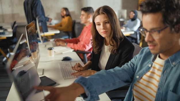 Diverso grupo multiétnico de estudiantes femeninas y masculinas sentadas en una sala de la universidad colaborando en proyectos escolares en una computadora Jóvenes académicos hablan de estudio Aplicar habilidades y conocimientos académicos en clase