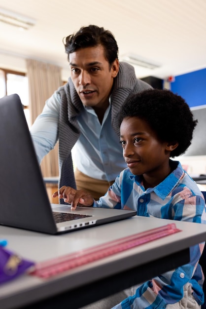 Foto diverso professor masculino usando laptop ensinando menino na sala de aula da escola primária