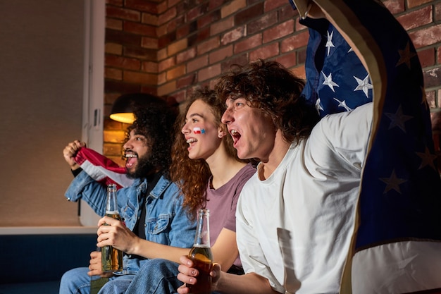 Diversos aficionados al deporte celebran la victoria en casa. Los partidarios apasionados gritan viendo el juego en la televisión, vitoreando juntos, gritando emocionalmente