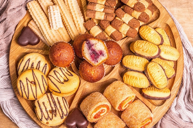 Diversos biscoitos e muffins variados. Placa de combinação de madeira na mesa de tábuas antigas, vista superior