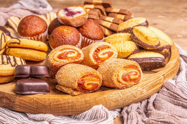 Diversos biscoitos e muffins variados. Placa de combinação de madeira na mesa de tábuas velhas, close-up