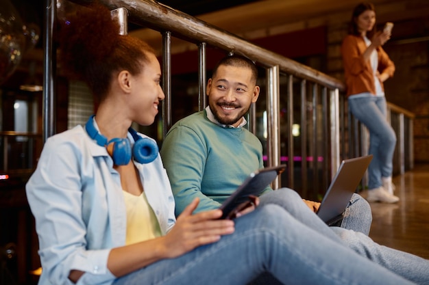 Diversos colegas de trabalho sentados no chão conversando enquanto usam tablets digitais