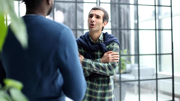 Diversos colegas masculinos en el corredor de la oficina moderna jóvenes hombres de negocios afroamericanos y caucásicos discutiendo el trabajo del proyecto común reunión en el trabajo de la compañía