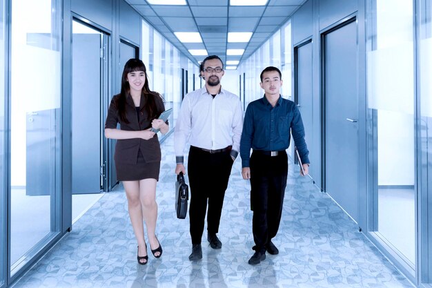 Diversos empresários olham para a câmera enquanto caminham juntos no corredor do escritório