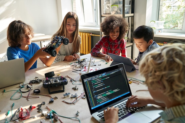 Diversos estudiantes escolares construyen autos robóticos usando computadoras y codificación