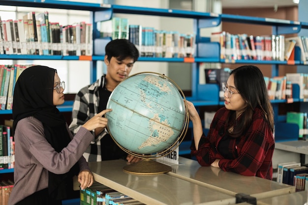 diversos estudiantes universitarios mirando el globo terráqueo aprendiendo geografía juntos en la biblioteca escolar