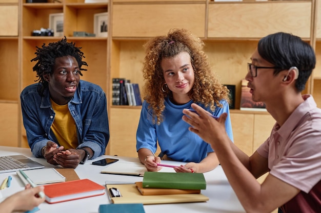 Foto diversos grupos de estudantes trabalhando juntos na biblioteca se concentram em uma jovem sorridente com cabelos cacheados