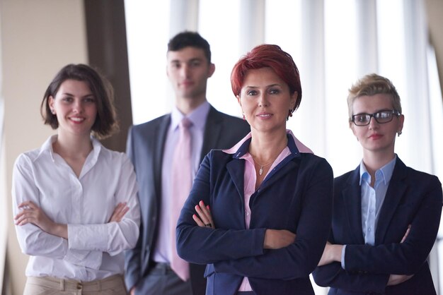 diversos grupos de personas de negocios de pie juntos como equipo en el moderno y luminoso interior de la oficina con una anciana pelirroja al frente como líder