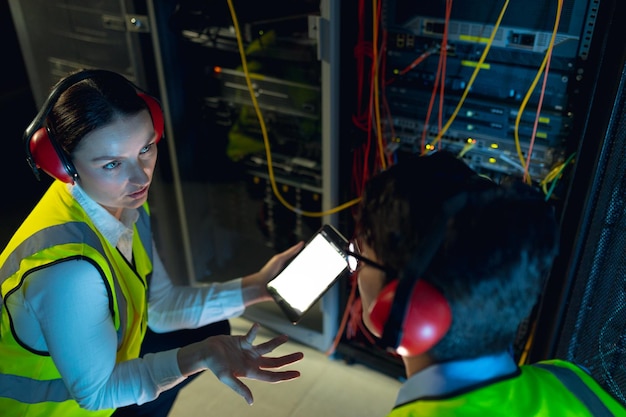 Diversos ingenieros, hombres y mujeres, que utilizan tabletas digitales mientras inspeccionan la sala de servidores de computadoras. concepto de gestión y mantenimiento del servidor de bases de datos