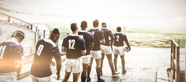 Diversos jogadores masculinos de rugby em pé na entrada do estádio em uma fileira para o jogo