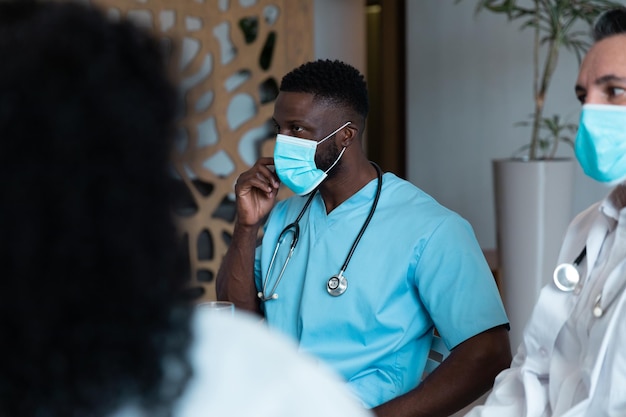 Diversos médicos, hombres y mujeres, con máscaras faciales sentados en el pasillo del hospital discutiendo