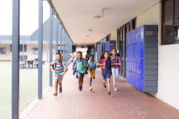 Foto diversos niños felices con bolsas de escuela corriendo en el espacio de copia del corredor de la escuela primaria