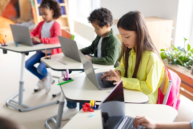 Diversos niños que usan computadoras portátiles en la clase de computación de la escuela primaria aprenden computación