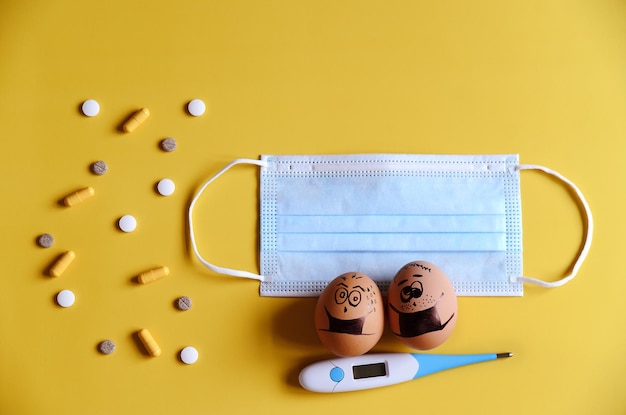 Diversos ovos de galinha com rostos de rabiscos usando máscaras médicas em fundo amarelo. Vírus corona