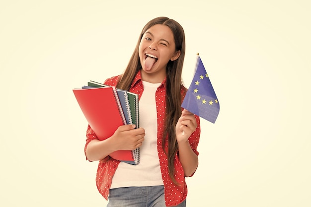 Divertida adolescente sostiene la bandera de la unión europea y el cuaderno escolar para estudiar de regreso a la escuela