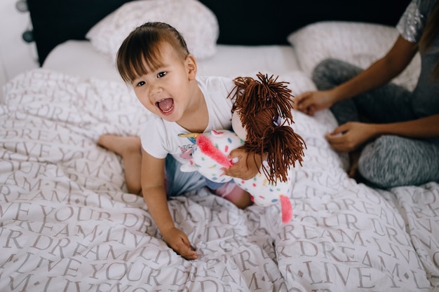 Divertida chica asiática jugando con una muñeca en casa