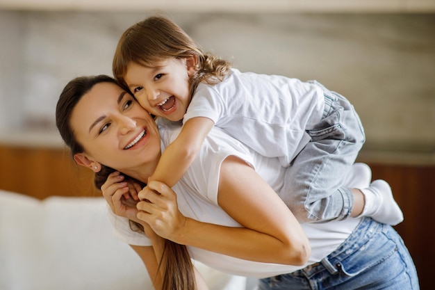 Foto divertida com o bebé feliz mãe a brincar com a adorável filha pequena em casa