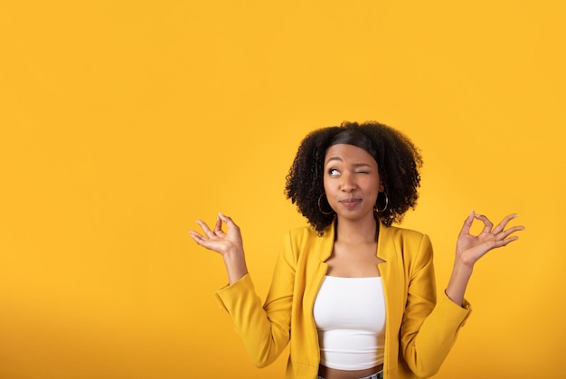 Divertida dama curiosamente negra mirando con un ojo al espacio libre meditando aislado en amarillo