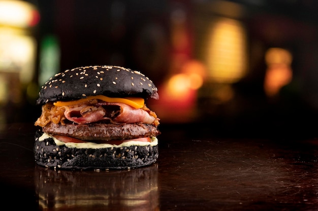 Foto divertida hamburguesa gorda con temática de halloween crujiente panecillo negro tocino y rodajas de cebolla con sésamo en la mesa de madera vista angular en la esquina con pub dssfocused en el fondo