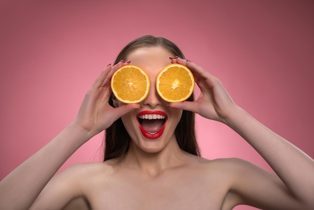 Divertida hermosa belleza modelo mujer joven sosteniendo dos jugosas rodajas de naranja como sus ojos o gafas char ...