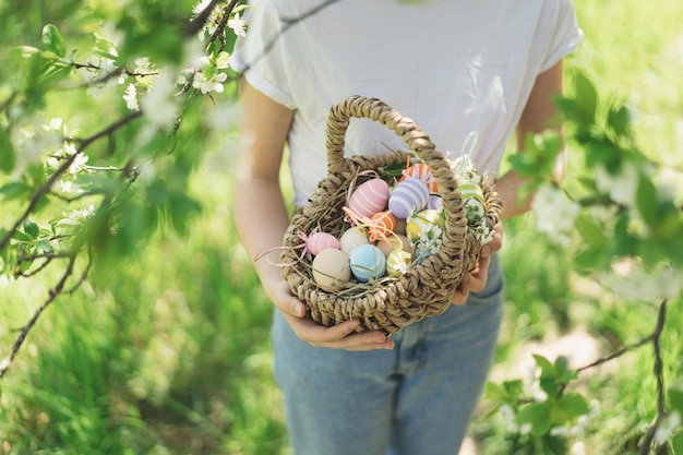 Divertida jovencita con canasta de huevos y orejas de conejo en la búsqueda de huevos de pascua en el soleado jardín de primavera