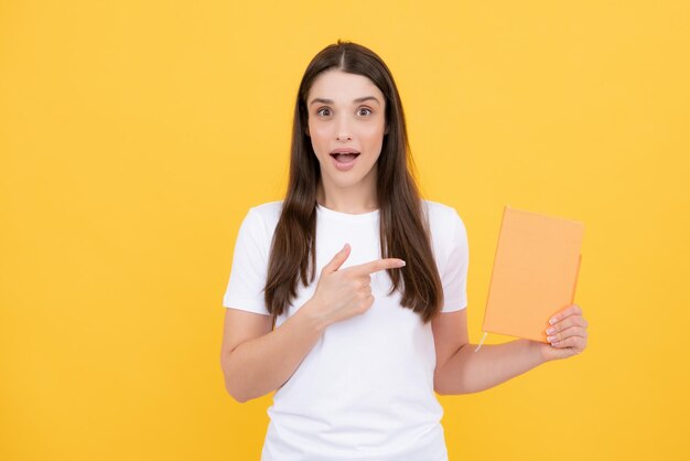 Divertida jovencita sorprendida con cuadernos de pie sobre fondo amarillo con espacio de copia Educativo