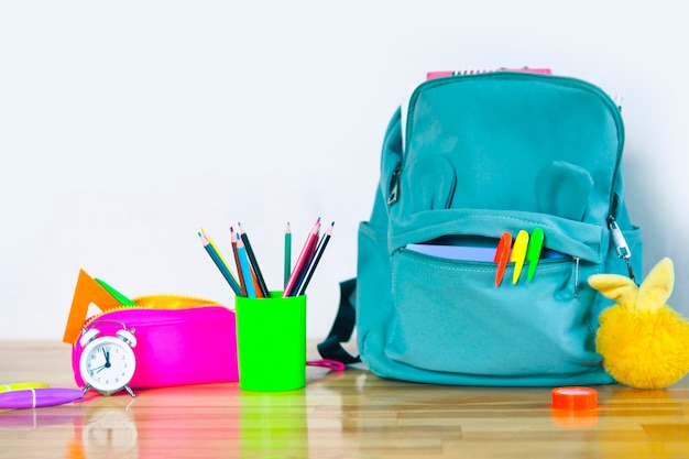 Divertida mochila escolar con rotuladores, estuche brillante, llavero de vidrio esponjoso con lápices de colores y un reloj despertador en una mesa de madera. volver al concepto de escuela.