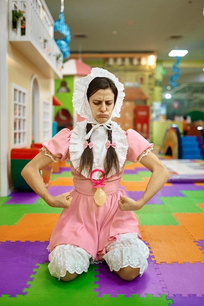 Divertida mujer linda vestida como un bebé recién nacido que muestra un fuerte músculo del brazo sobre la guardería infantil