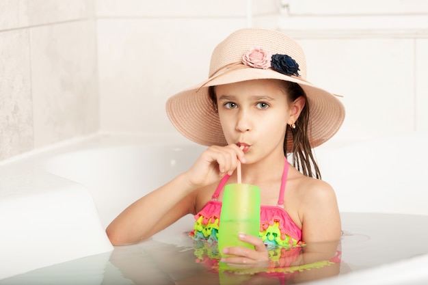 Divertida niña hermosa caucásica con sombrero juega playa bañándose en casa