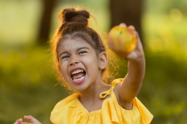 Foto divertida niña morena está comiendo manzana en el jardín refrigerio saludable para niños concepto de verano