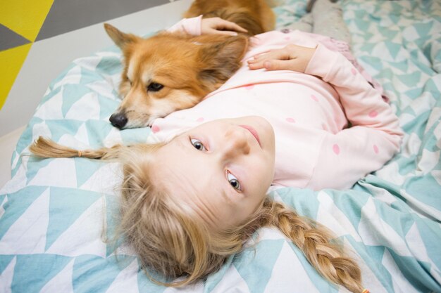 Divertida niña y perro corgi en la cama en la guardería.